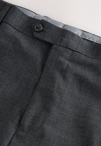 Pantalon de costume gris foncé avec une taille boutonnée et une doublure intérieure grise visible sur le bord supérieur.