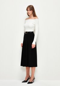 Off-shoulder vit ribbad topp i kombination med en svart veckad midikjol; svart bälte med metalliska detaljer; svarta spetsiga klackar.