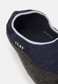 Chaussons en laine avec un extérieur gris foncé, une doublure texturée bleu marine et des bordures bleu clair, portant une étiquette noire avec le mot 'FALKE' sur le côté.