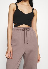 Top corto nero con scollatura a V e spalline sottili, abbinato a pantaloni della tuta rosa chiaro con cordoncino realizzati in tessuto morbido.
