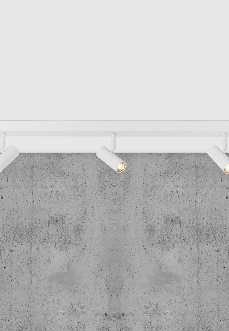 Drei weiße, an der Decke montierte Strahler beleuchten eine strukturiert graue Betonwand.