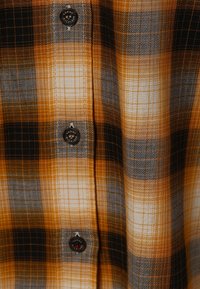 Camisa a cuadros con una combinación de colores naranja, negro y gris. Fabricada con una tela de textura suave y terminada con botones negros.