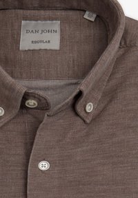 Camisa marrón de botones con una tela texturizada. Presenta un collarete tradicional, botones blancos y una etiqueta que dice "DAN JOHN REGULAR."