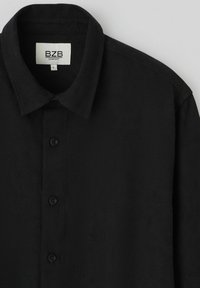 Chemise noire à boutons avec un motif texturé, dotée d'un col et de six boutons, fabriquée en tissu léger. L'étiquette indique "BZB Comfort, L."