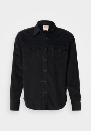 Camisa de corduroy negra de manga larga con botonadura frontal, dos bolsillos de solapa en el pecho con botones y cuello puntiagudo.