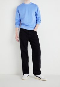 Sudadera azul clara con cuello redondo y puños acanalados, combinada con pantalones negros de pierna recta y zapatillas blancas con detalles en azul marino.