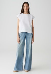 Witte top met korte mouwen en kanten details op de schouders, in combinatie met lichtblauwe wijde jeans. Soepele textuur, casual pasvorm, neutrale kleuren.