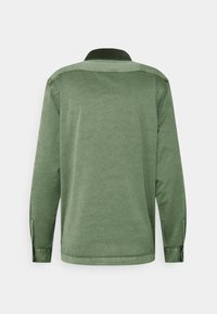 Langärmliges Hemd aus weichem olivgrünem Stoff, mit Kragen, geknöpften Manschetten und geradem Saum. Unverziert ohne Muster.