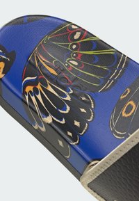 Design de papillon multicolore sur un fond texturé bleu, avec des accents noirs et une forme courbée lisse. Le côté présente un bord noir mat.
