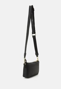 Musta nahkainen olkalaukku, jossa on teksturoitu pinta. Varustettu kultaisella vetoketjulla ja säädettävällä hihnalla, jota korostaa hienovarainen logo-kuvio.
