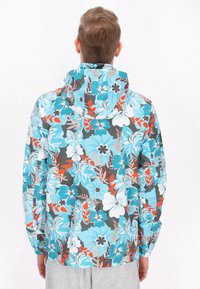 Bloemenregenjas met een capuchon, met een blauwe achtergrond, grote witte en rode bloemen, en elastische manchetten. Soepele, lichte stof.