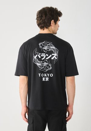 Zwarte katoenen t-shirt met een witte grafiek van twee koi-vissen en Japanse tekst op de achterkant. Korte mouwen en een relaxte pasvorm.