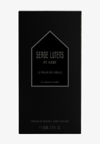 Scatola nera con testo argentato. Il testo include "Serge Lutens", "a casa" e "Le Palais des Sables". Dimensione: 100ml. Design minimalista.