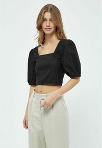 Must värvitud lühike crop-top ruudukujulise kaelusega, punnitatud lühikeste varrukatega ja sileda tekstuuriga, koos heledate beežide kõrge vöökohaga pükstega.
