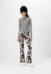 Gray knitted top with a keyhole detail, paired with black and white spotted flared trousers. White pointed heels and a black furry hat.