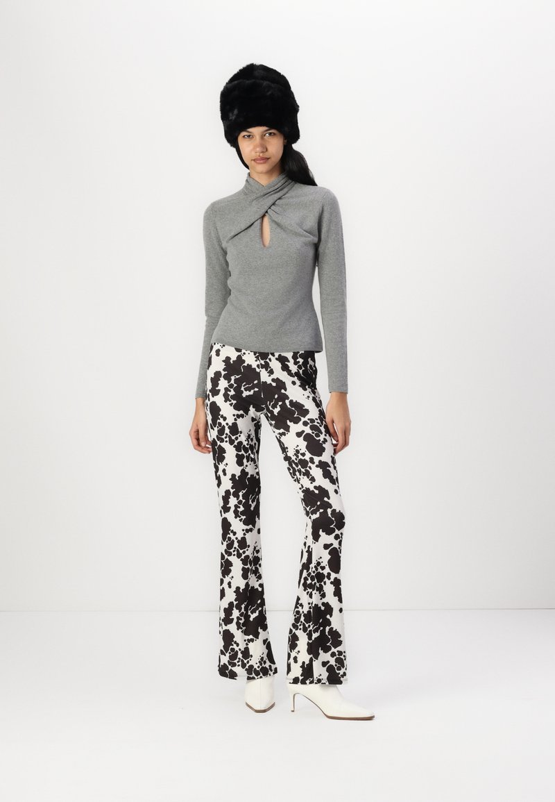 Grüner gestrickter Pullover mit einem Schlüsselloch-Detail, kombiniert mit schwarzen und weißen gepunkteten Schlaghosen. Weiße spitze Absätze und ein schwarzer pelziger Hut.