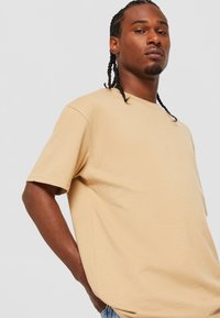 Tricou cu mânecă scurtă, guler rotund, din bumbac bej deschis. Croi drept, cu o textură netedă și detalii cu cusături laterale.