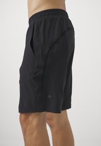 Svarta sportshorts med texturerad yta, elastisk midja, sidofickor och en diskret logga nederst på fållen.