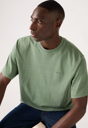 Green cotton t-shirt with a crew neckline and short sleeves. Features subtle logo detail on the chest and a soft, textured fabric.