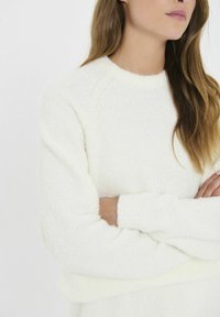Bela puhasta majica s krojem okruglega izreza, raglan rokavi in mehak material, z zavihanimi manšetami in udobnim prileganjem.