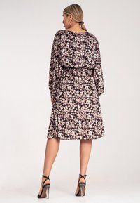 Kwiatowa sukienka z czarnym tłem, na którym znajdują się różowe i białe kwiaty, długie rękawy i wcięcie w talii. Noszona z czarnymi szpilkami.