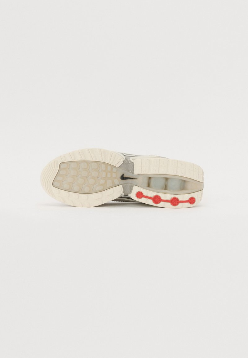 Zapatilla con una mediasuela transparente, parte superior gris, suela de goma blanca y acentos circulares rojos a lo largo del costado. Superficie texturizada para mayor agarre.