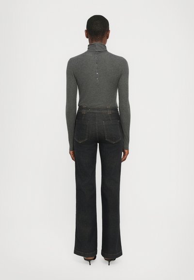 Pelēks turtlenecks tops ar poga aizdari aizmugurē, apvienots ar tumšiem izplešamajiem džinsiem, kuriem ir divas aizmugures kabatas un kontrastējoša dūkošana.