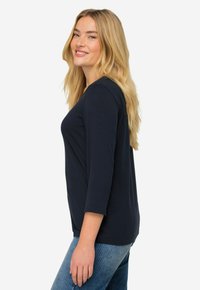 Navyblaues Langarmshirt mit rundem Halsausschnitt und lässigem Schnitt, kombiniert mit hellblauen Denim-Jeans. Glatte Textur, keine Muster.