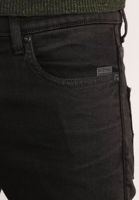 Vaqueros de mezclilla negros con un diseño clásico de cinco bolsillos, costuras sutiles y un pequeño parche del logo de G-Star en el bolsillo delantero.