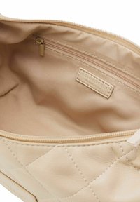 Interno della borsa in pelle quilted beige con rivestimento in tessuto liscio, dotato di una tasca con zip e un'etichetta del marchio impresso sul lato.