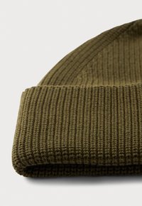 Bonnet en tricot vert olive avec revers, texture côtelée, posé sur une surface blanche.