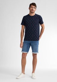 Laivastön sininen lyhythihainen T-paita, jossa on pieni punainen lehtipainatus, yhdistettynä vaaleansinisiin farkkushortseihin ja valkoisiin tennareihin; rento istuvuus ja rento tyyli.