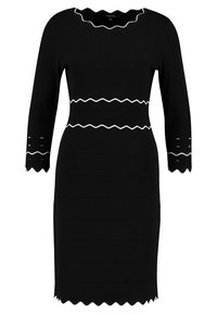 Svart ribbad klänning med långa ärmar, scallopad halsringning och vit zigzag-detaljering över midjan och ärmarna, texturerad tyg.