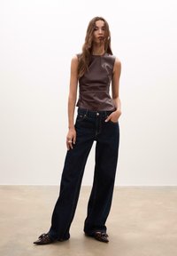 Brun læder ærmeløs top med en tætsiddende design, parret med mørkeblå bredbenede denim jeans med synlige syninger og lommer.