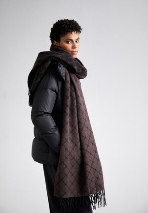 Brown patterned scarf made of soft fabric, draped around the neck. Features a geometric design and frayed edges, paired with a black puffer jacket.