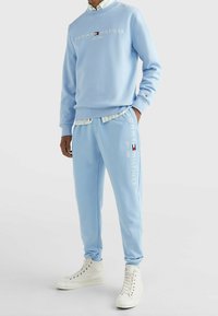 Ljusblå bomullströja med rund halsringning och broderad logotyp; matchande sweatpants med logotypdetalj och elastiska muddar; vita sneakers.