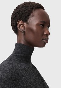 Tummanharmaa korkeakauluksinen neulepaita, jossa on teksturoitu pinta ja sivussa nappikoristelu, yhdistetty yksinkertaiseen korvakoruun.