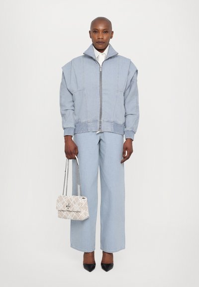 Giubbotto in denim azzurro chiaro oversize con collo alto, chiusura con zip e polsini a coste, abbinato a pantaloni a gamba larga coordinati e una borsa con fantasia.