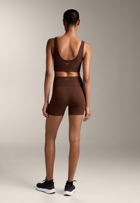 Soutien-gorge de sport marron à côtes et shorts taille haute assortis, avec une coupe ajustée et des coutures minimales. Chaussures de sport noires.