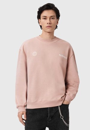 Sweatshirt rose clair en tissu doux, doté d'un col rond, de manches longues et de logos blancs imprimés sur la poitrine et la manche.