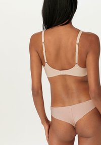 Beige beha met verstelbare bandjes en haaksluiting, gecombineerd met bijpassend bikinicut ondergoed. Gladde, zachte stof, minimalistisch ontwerp.