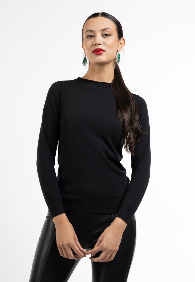 Sort langærmet sweater lavet af blødt stof, med rund halsudskæring og tætsiddende design, kombineret med sorte læderbukser.