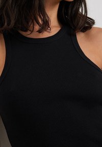 Débardeur noir côtelé avec une coupe près du corps et un col haut. Le tissu présente une apparence texturée et une finition douce.