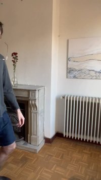 Inimene kõndimas mööda dekoratiivset kivist kaminat, millel on klaasvaas punaste lilledega, lähedal valge radiaator ja abstraktne seinamaal.