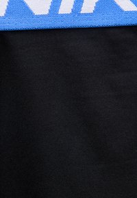 Nærbilde av stoff som viser en svart strikket tekstur med en blå og hvit trykt kantdetalj øverst.