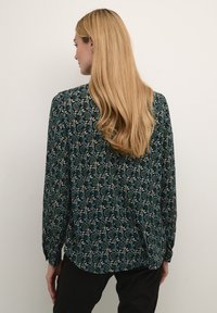 Langærmet bluse i mørk teal med intrikate blomster mønstre i creme og lyse teal. Blødt stof med en afslappet pasform og rygplissédetalje.
