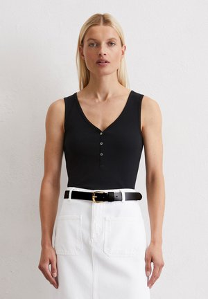Schwarzer ärmelloser Body mit V-Ausschnitt und Dreiknopfverschluss, kombiniert mit einem weißen Jeansrock und einem schwarzen Gürtel mit goldener Schnalle.