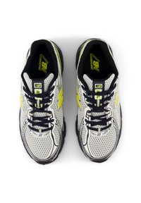 Bílé sportovní boty z prodyšné síťoviny s černými detaily, žlutým logem a černými tkaničkami. Mají polstrovanou podrážku a elegantní design.