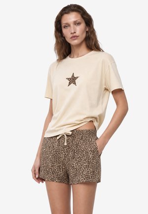 Jonge vrouw die een beige T-shirt met een luipaardprint ster draagt en bijpassende luipaardprint shorts met een taillekoord.