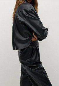 Chaqueta corta de imitación de cuero negra con mangas largas, textura suave y corte relajado, combinada con pantalones de talle alto a juego.